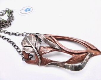 May include: A silver chain necklace with a copper and silver pendant featuring a stylized leaf design.