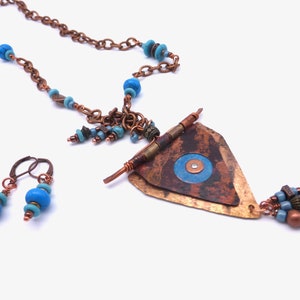 May include: A copper necklace with a triangular pendant featuring a blue and white eye design. The necklace is adorned with blue and turquoise beads. Matching earrings with blue beads are also included.