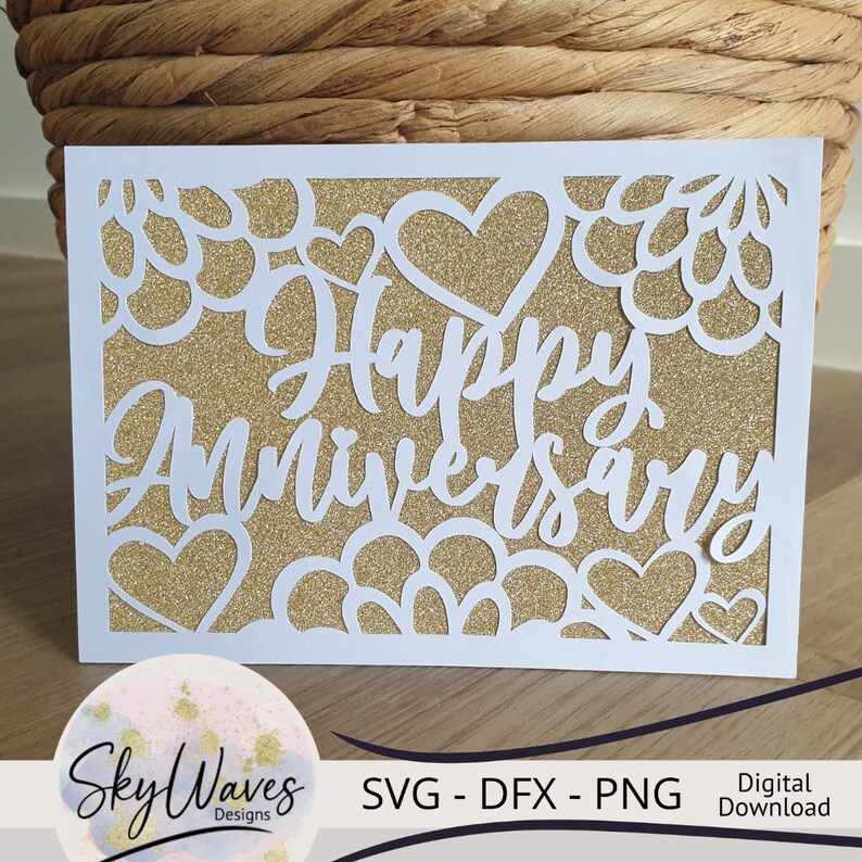 Op de afbeelding: Witte kaart met een gouden glitterachtergrond en een wit uitgesneden ontwerp van harten en bloemen. De tekst "Happy Anniversary" is geschreven in een wit cursief schrift.