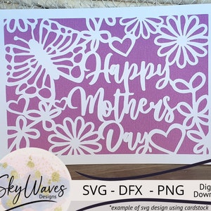 May include: A white card with a purple gradient background and a white cut-out design of flowers and hearts. The text "Happy Mothers Day" is cut out in white.