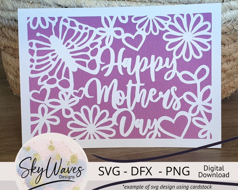 May include: A white card with a purple gradient background and a white cut-out design of flowers and hearts. The text "Happy Mothers Day" is cut out in white.