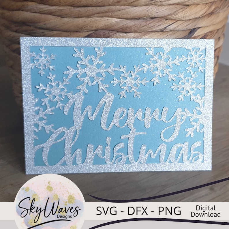 K&ouml;nnte beinhalten: Hellblaue Weihnachtskarte mit silbernem Glitzerrahmen und Schneeflocken. Die Worte "Merry Christmas" sind in einer kursiven Schriftart ausgeschnitten. Das Logo "SkyWaves Designs" und der Text "SVG - DFX - PNG" sind ebenfalls zu sehen.