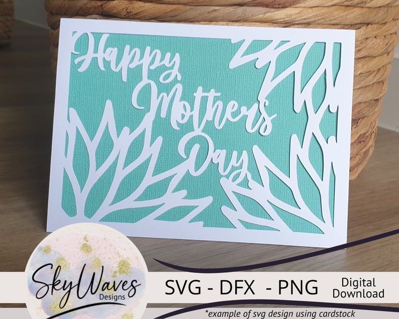 May include: A white card with a teal background and a cut-out design of leaves and the text "Happy Mother's Day". The card is on a wooden surface. The text "SVG - DFX - PNG Digital Download" is below the card.