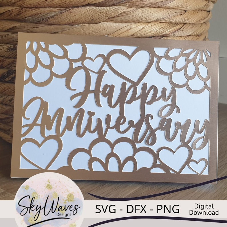 Op de afbeelding: Een gouden kaart met een witte achtergrond en een uitgesneden ontwerp van harten en bloemen. De tekst "Happy Anniversary" is geschreven in een gouden handschrift.