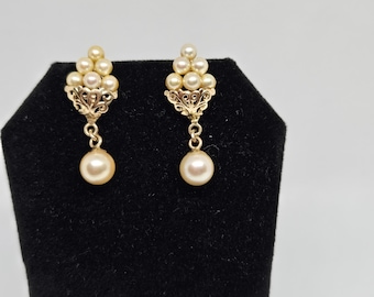 May include: A pair of gold earrings with a cluster of small pearls at the top and a single larger pearl dangling from the bottom.