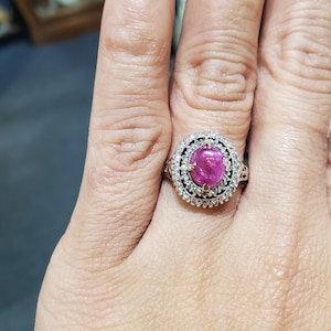 May include: A silver ring featuring a large oval pink gemstone encircled by a double halo of smaller clear gemstones.