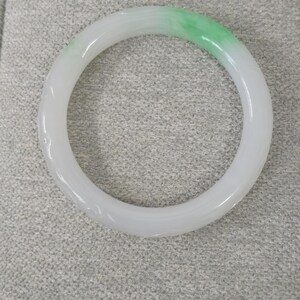 May include: A jade bangle bracelet, featuring a smooth, polished surface. The bracelet transitions from a white hue to a vibrant green. This piece of jewelry is a circular, solid band, showcasing a natural stone aesthetic.