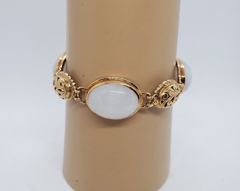 May include: A gold bracelet with three white oval-shaped stones. The bracelet has a detailed floral design.