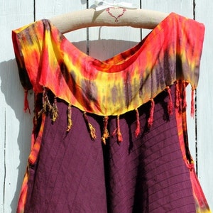 Puede incluir: Un top sin mangas de tie-dye con una falda burdeos. El top tiene un patrón de tie-dye amarillo, naranja y rojo con borlas alrededor del escote. La falda es de color burdeos sólido con un patrón de rombos.