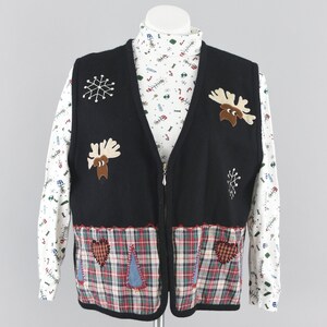 May include: A black sleeveless vest with a front zipper, featuring embroidered moose and snowflake motifs, layered over a white long-sleeve turtleneck shirt with a multi-colored holiday print and a plaid hemline with heart and tree appliques.