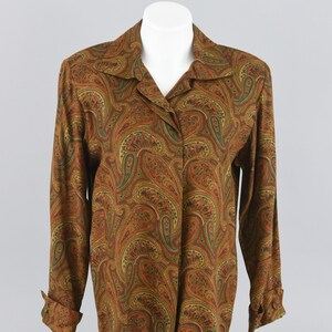 May include: A long-sleeved button-down shirt featuring a dense, multi-colored paisley pattern in shades of burnt orange, deep green, and gold. The shirt has a classic collar, a straight hemline, and cuffs that are folded upward at the wrists.
