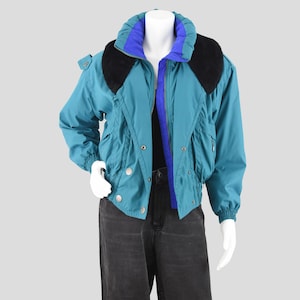 May include: A teal jacket featuring a high collar with a bright blue inner lining and black faux fur trim. The jacket includes a front zipper closure, snap buttons, long sleeves with elastic cuffs, and a cinched waist, worn over black denim jeans.