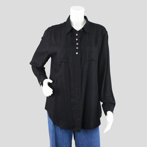 May include: A black button-down shirt with long sleeves, two chest pockets, and pearl-like buttons. The shirt is displayed on a mannequin, paired with blue jeans. The collar is pointed, and the cuffs have buttons.