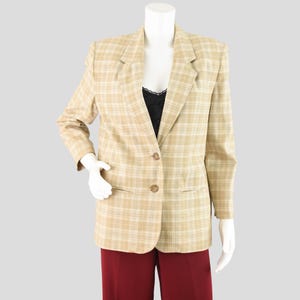 May include: A tan plaid blazer with a two-button closure, set on a mannequin. The blazer has a classic notched lapel and two front pockets. The mannequin is wearing a black top and burgundy pants.