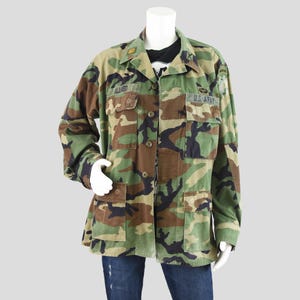 May include: Camouflage pattern jacket with multiple pockets and button closures. The jacket features the name "ALLRED" above the left chest pocket and "U.S. ARMY" on the right chest. The jacket is displayed on a mannequin.