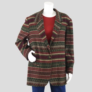 May include: A patterned blazer in shades of green, burgundy, and tan. The blazer features a geometric design and a single-button closure. The garment is displayed on a mannequin, showcasing its tailored fit and style. The blazer has two front pockets.