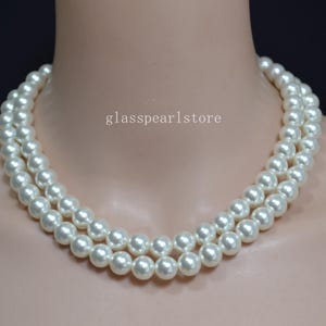 Puede incluir: Un collar de perlas de doble hebra de color blanco cremoso. El collar está drapeado alrededor de un cuello, con el texto "glasspearlstore" visible.