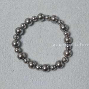 May include: A silver gray pearl bracelet with a simple design. The bracelet is made of round pearls that are strung together on a clear elastic cord.
