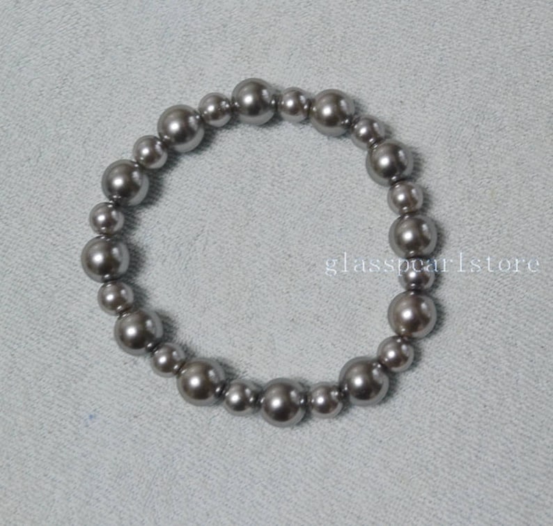 May include: A silver gray pearl bracelet with a simple design. The bracelet is made of round pearls that are strung together on a clear elastic cord.