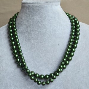 May include: A double strand necklace made of dark green faux pearls. The necklace is displayed on a gray mannequin.