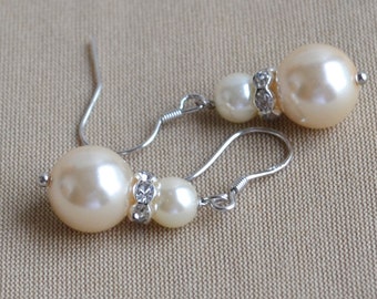 May include: A pair of silver earrings with two white pearls and a rhinestone accent.