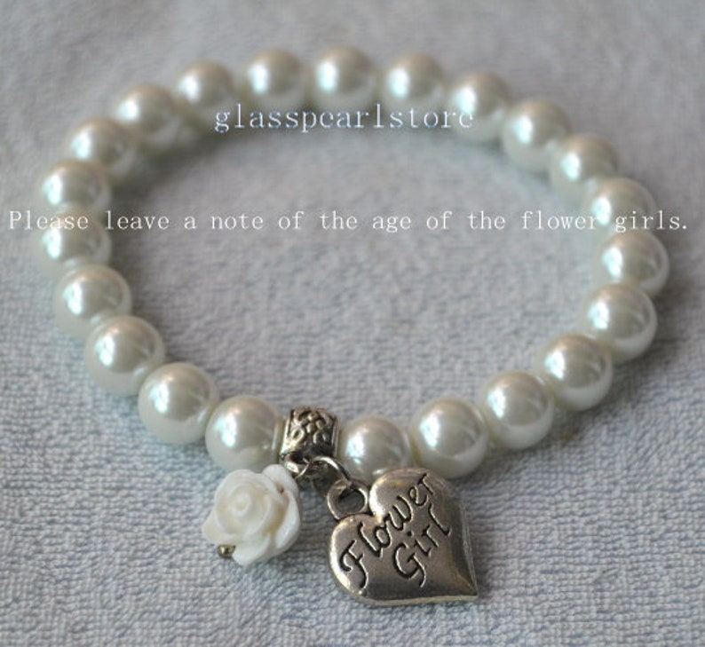 May include: White pearl bracelet with a silver charm that says "Flower Girl". The charm is attached to a white flower.