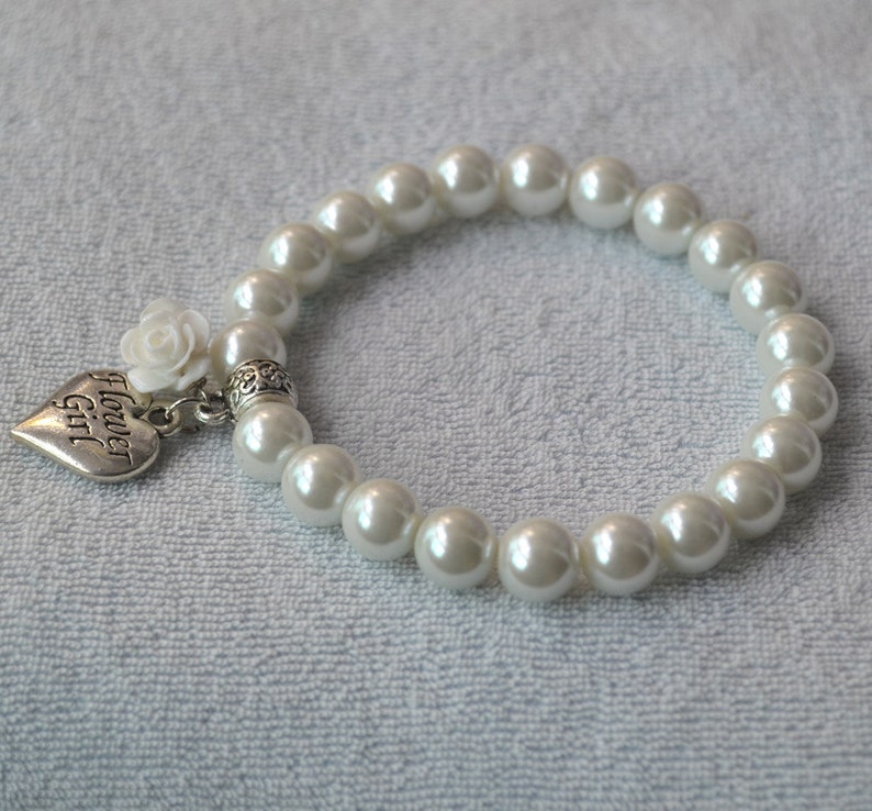 May include: White pearl bracelet with a silver heart charm that says "Flower Girl". The charm also has a small white flower attached.