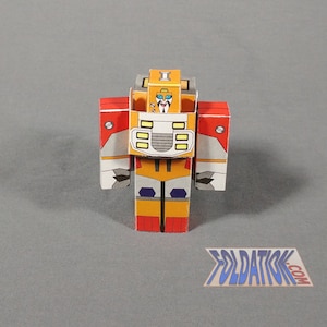 以下が含まれることがあります： オレンジ、赤、白、グレーの色の紙製のロボットモデル。ロボットは、黄色のヘルメットと青い口をした顔をしています。ロボットは灰色の表面に立っています。画像の右下隅に「FOLDATICK.COM」というテキストが表示されています。