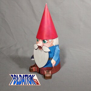 May include: A papercraft gnome with a red hat, white beard, and blue shirt. The gnome is standing with its legs slightly apart and its arms at its sides. The gnome is made of paper and has been cut out and folded to create a three-dimensional figure.