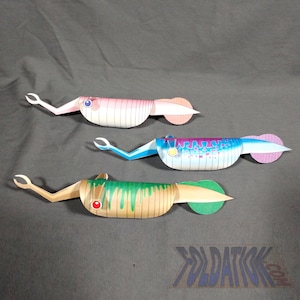 May include: Three papercraft models of squid-like creatures with different color schemes. The first is pink and white, the second is blue and purple, and the third is green and brown. Each model has a pair of arms and a tail fin.