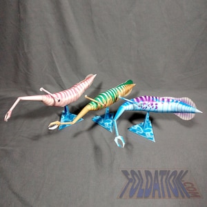 May include: Three papercraft models of prehistoric marine animals, each with a different color scheme. The first is pink and white, the second is green and yellow, and the third is blue and white. All three models are on blue and white bases.