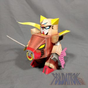 May include: A papercraft model of a red and yellow robot with a sword and a pink and white scarf. The robot has a bull's head and a yellow helmet with a blue visor. The model is made of paper and is folded into a three-dimensional shape.