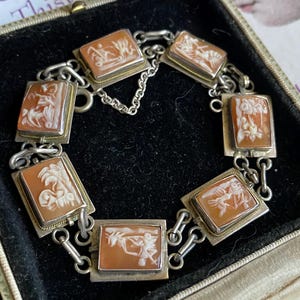 May include: A vintage bracelet featuring rectangular cameo stones with classical figures. The stones are set in silver-toned metal with gold accents and linked together. The bracelet is presented in a black velvet-lined box.
