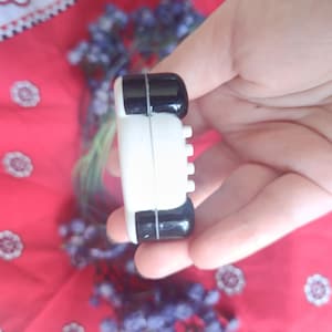 May include: A small, rectangular, two-toned object featuring a glossy black top and bottom section separated by a white centre band. The white section displays a series of four small, evenly spaced, protruding white circular buttons on the side.
