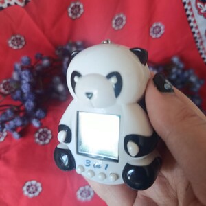 May include: A white and black panda-shaped digital handheld game device with a small square screen. The front of the device features the text 3 in 1 printed in blue above three small white circular buttons. The panda has black ears, eyes, and paws.