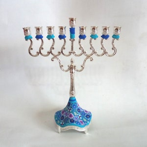 May include: Silver menorah with nine candle holders and a blue and white floral patterned base.