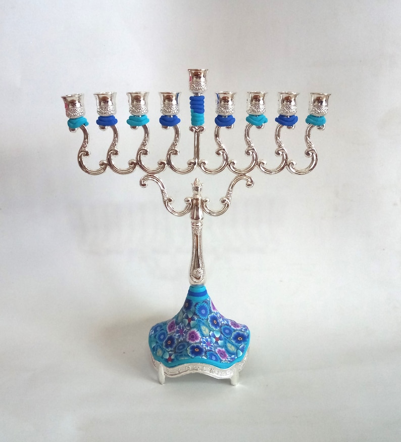 May include: Silver menorah with nine candle holders and a blue and white floral patterned base.