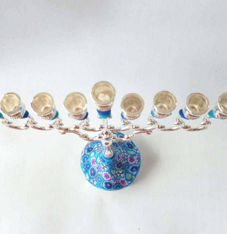 May include: Silver menorah with a blue and white floral base. The menorah has nine candle holders and is decorated with blue and silver accents.