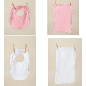 May include: Four baby bibs hanging on a clothesline. Two are pink with ruffled edges and two are white with ruffled edges.