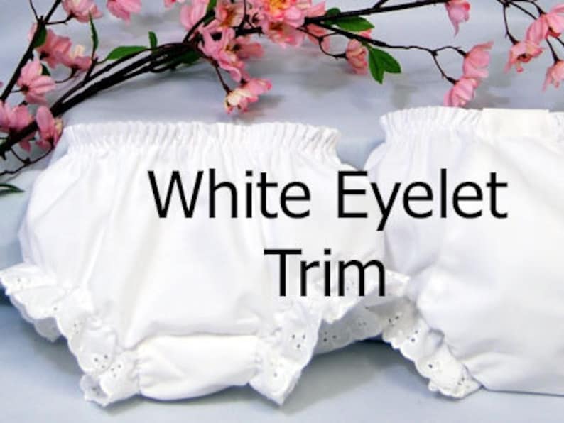 May include: Two white cotton baby bloomers with white eyelet trim. The bloomers have a gathered elastic waistband and a ruffled edge. The text "White Eyelet Trim" is superimposed on the image.