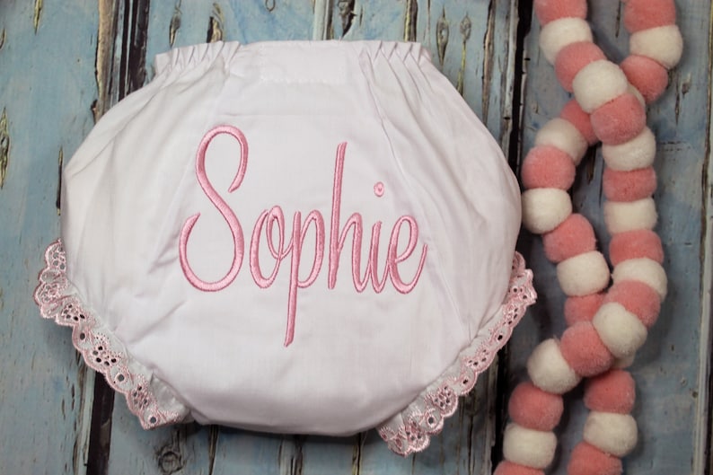 May include: White baby bloomers with pink lace trim and the name "Sophie" embroidered in pink.