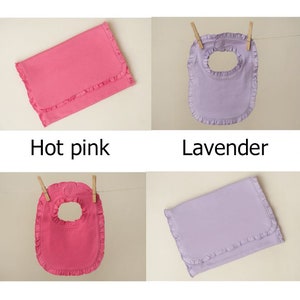 May include: Four baby bibs in two colors: hot pink and lavender. Two bibs are folded flat, and two bibs are hanging from clothespins. All bibs have a ruffled edge.