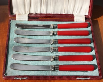 Boxed set of six silver plated tea knives with red celluloid handles.