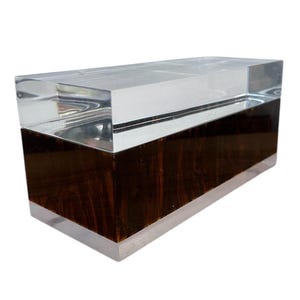 May include: A rectangular clear acrylic box with a dark brown wood inlay. The box is made of two pieces of acrylic, one on top of the other, with the wood inlay sandwiched between them.