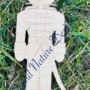 May include: Wooden cutout of a mouse dressed as a nutcracker soldier. The mouse has a crown on its head and is holding a sword. The cutout is unfinished and ready to be painted.