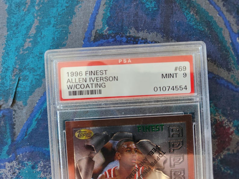 May include: A graded Allen Iverson 1996 Finest basketball card, encased in a protective holder. The card is graded MINT 9 by PSA, with the serial number 01074554. The card features Allen Iverson and the Topps Finest logo.