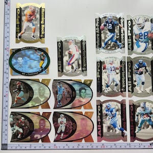 Puede incluir: Una colección de cromos de fútbol que muestran a varios jugadores en acción. Las tarjetas tienen un brillo metálico e incluyen texto como "All-Pro", "Quarterback" y "Running Back". Las tarjetas son de varias formas y tamaños.
