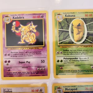 May include: Two vintage Pok&eacute;mon trading cards. The first card features Kadabra, a yellow creature with a spoon, and the second card features Kakuna, a yellow cocoon-like Pok&eacute;mon. Both cards are in protective sleeves.
