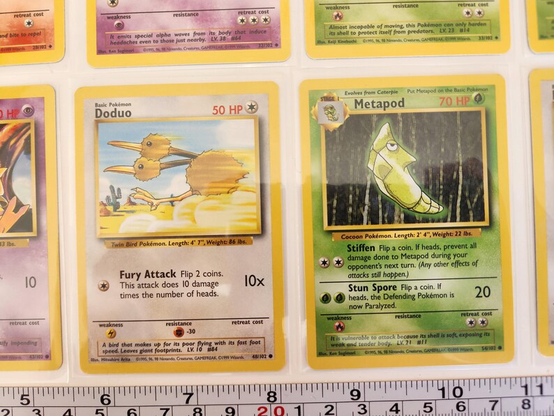 May include: Two Pok&eacute;mon trading cards, Doduo and Metapod, are displayed. Doduo, a twin bird, is depicted in brown and tan. Metapod, a cocoon Pok&eacute;mon, is shown in green. The cards are in protective sleeves.