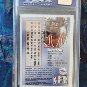 May include: A professionally graded Allen Iverson basketball card, encapsulated in a clear plastic case. The card features a photo of Iverson in a 76ers uniform, along with his collegiate record and other details. The card is labeled "69" and "A23".